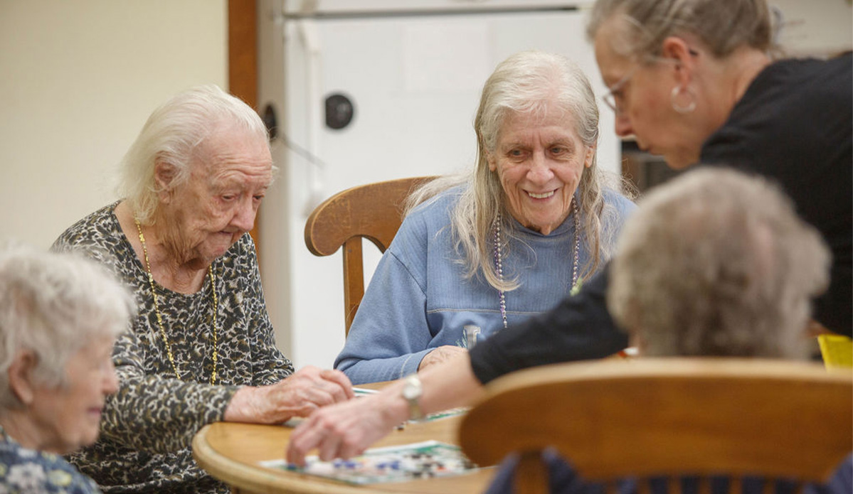 Three elderly women enjoying a lively game of dominoes at a table, smiling and engaged in friendly competition.