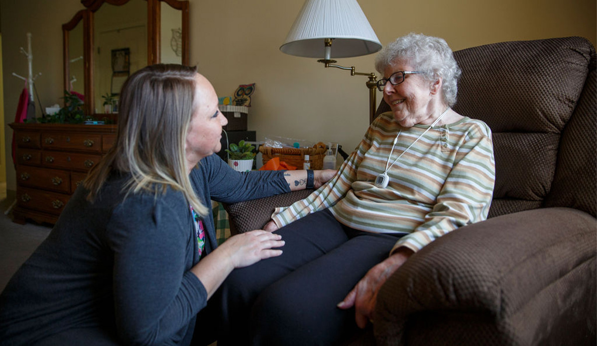 A woman in a chair chatting with an older woman, both engaged in a friendly conversation.