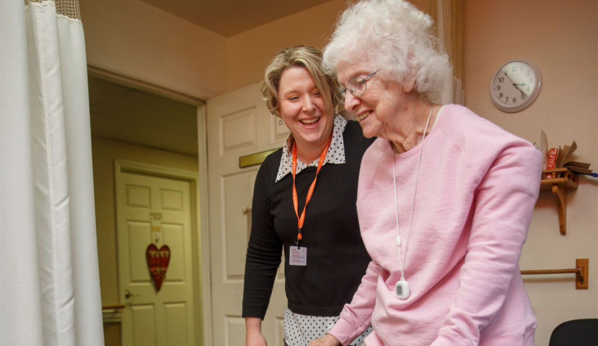 A woman in a wheelchair gently holds the hand of an older woman, sharing a moment of connection and support.