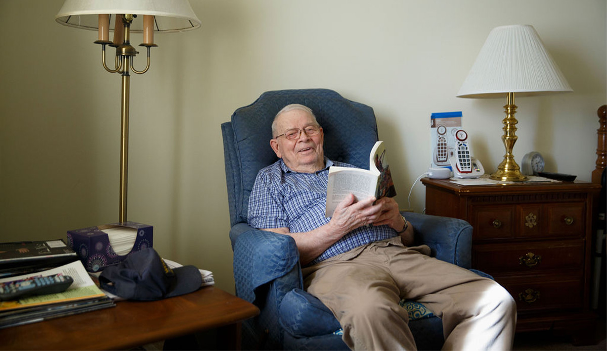 An older man sitting comfortably in a chair, deeply focused on reading a book.